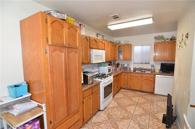 kitchen with visible vents, backsplash, brown cabinetry, white appliances, and a sink