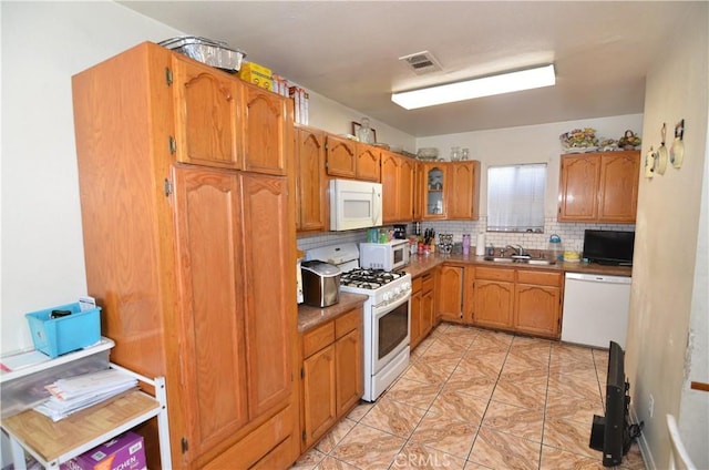 kitchen with tasteful backsplash, visible vents, a sink, white appliances, and brown cabinetry