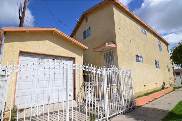 view of front of property with stucco siding, a garage, a gate, fence, and crawl space