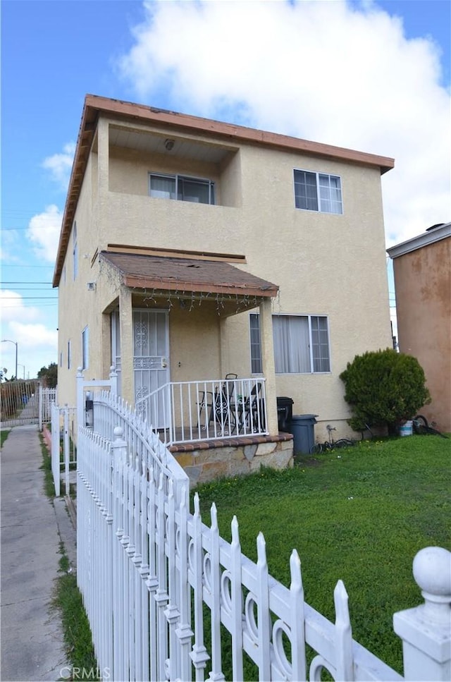 view of front of home with stucco siding, a porch, a fenced front yard, and a front lawn