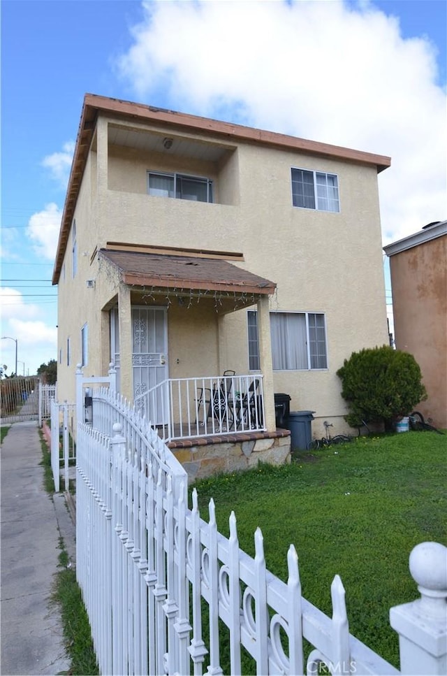 view of front of home with a porch, a fenced front yard, stucco siding, and a front lawn