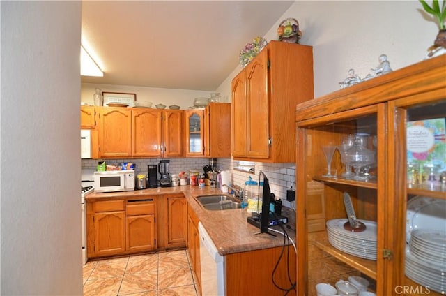 kitchen with a sink, tasteful backsplash, white appliances, brown cabinetry, and glass insert cabinets