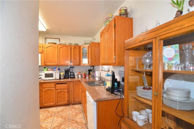 kitchen with brown cabinetry, decorative backsplash, white appliances, and a sink