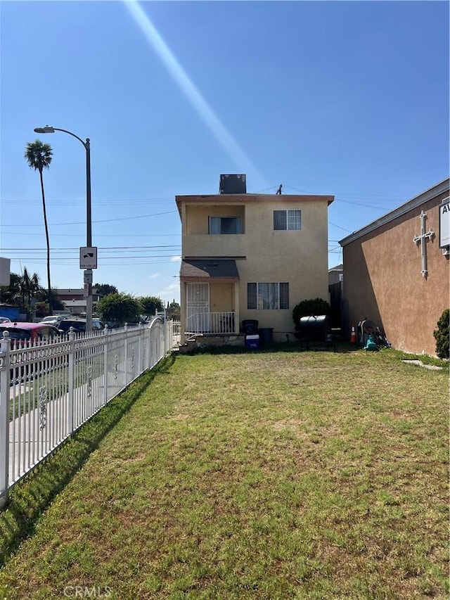 rear view of house with fence, a lawn, and stucco siding