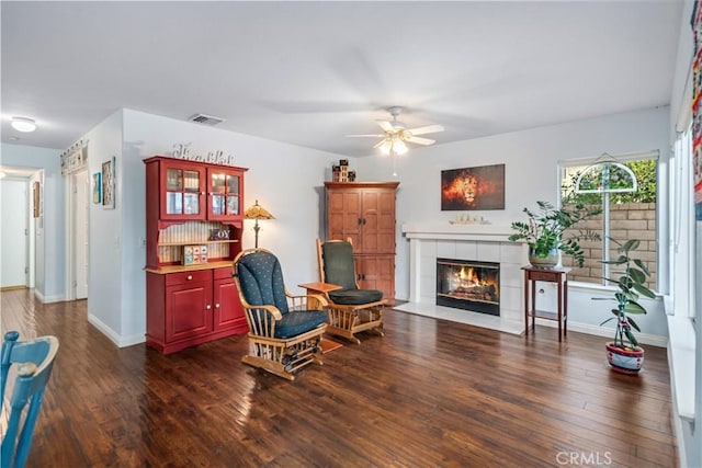 living area with visible vents, baseboards, a fireplace, dark wood-style floors, and a ceiling fan