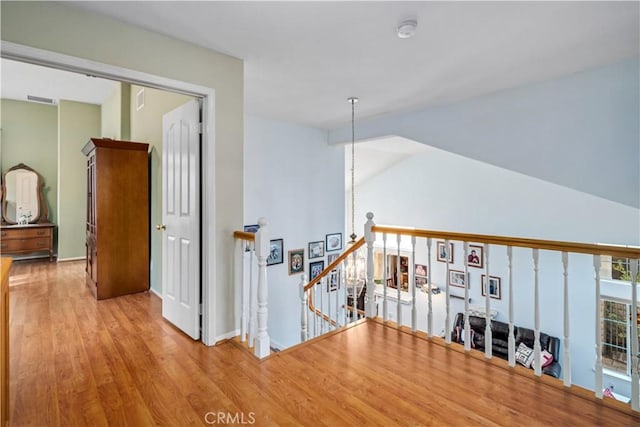 hallway featuring wood finished floors, an upstairs landing, visible vents, and vaulted ceiling