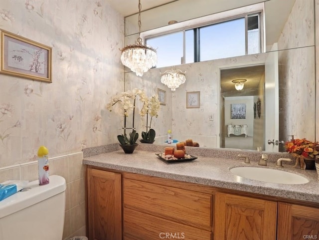 half bathroom featuring a notable chandelier, toilet, wallpapered walls, and vanity