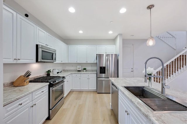 kitchen featuring light wood finished floors, appliances with stainless steel finishes, white cabinetry, and a sink