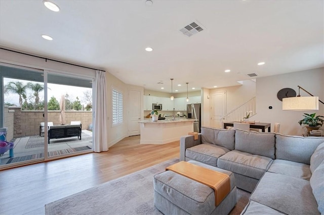 living area with recessed lighting, visible vents, light wood-style floors, and stairs