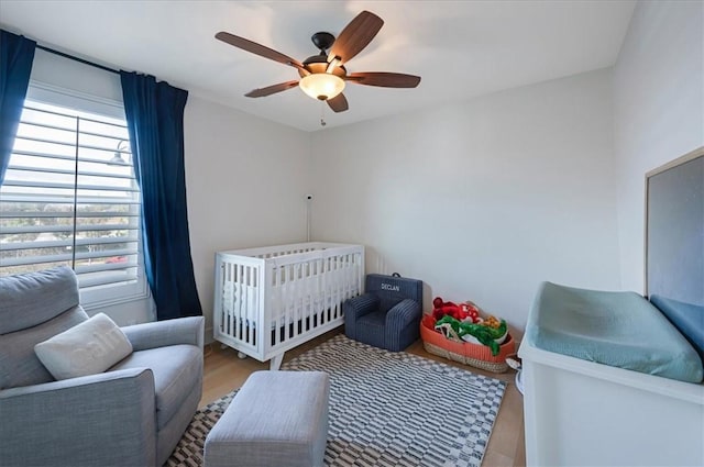 bedroom featuring a crib, wood finished floors, and a ceiling fan