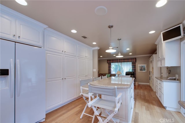 kitchen featuring visible vents, white refrigerator with ice dispenser, a center island, and white cabinetry