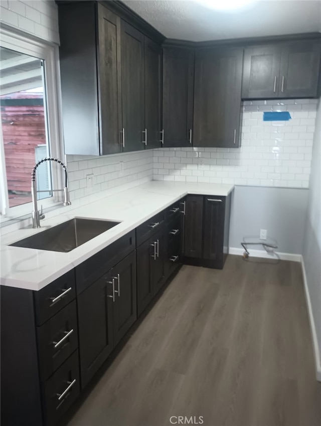 kitchen featuring wood finished floors, baseboards, backsplash, and a sink