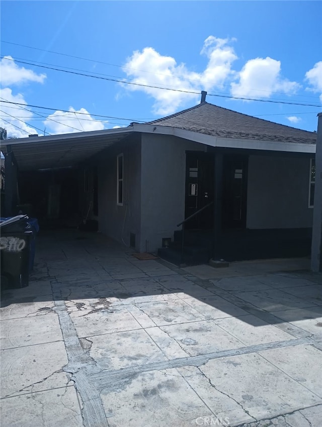 view of front facade featuring an attached carport, concrete driveway, roof with shingles, and stucco siding