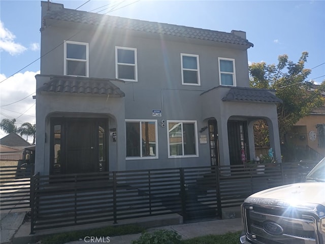 multi unit property featuring a fenced front yard, stucco siding, and a tile roof