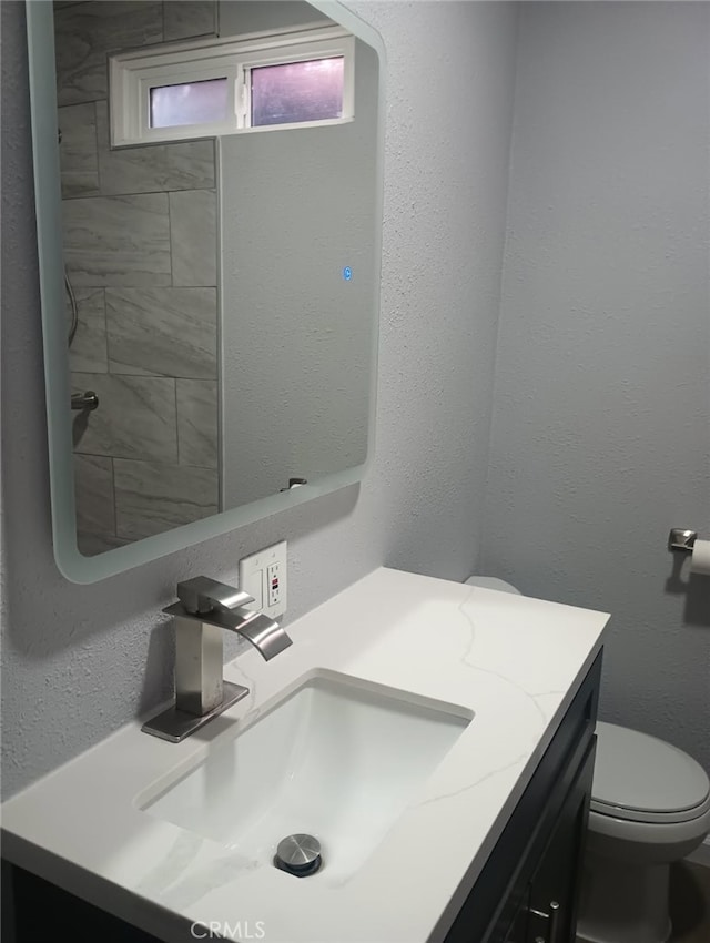 bathroom with toilet, vanity, and a textured wall