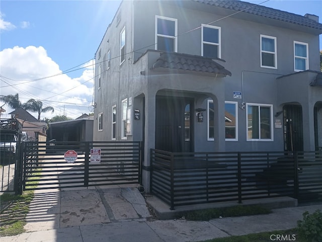 view of front facade featuring a tile roof, a gate, a fenced front yard, and stucco siding