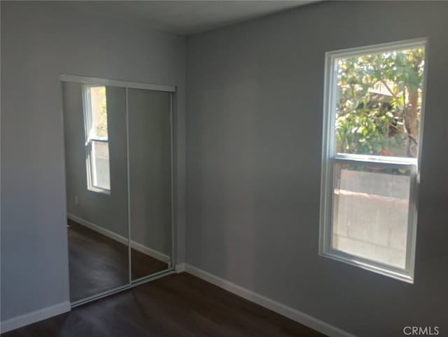 unfurnished bedroom featuring a closet, baseboards, and dark wood-style flooring