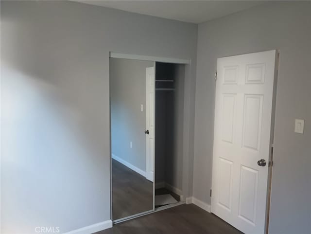 unfurnished bedroom with dark wood-type flooring, baseboards, and a closet