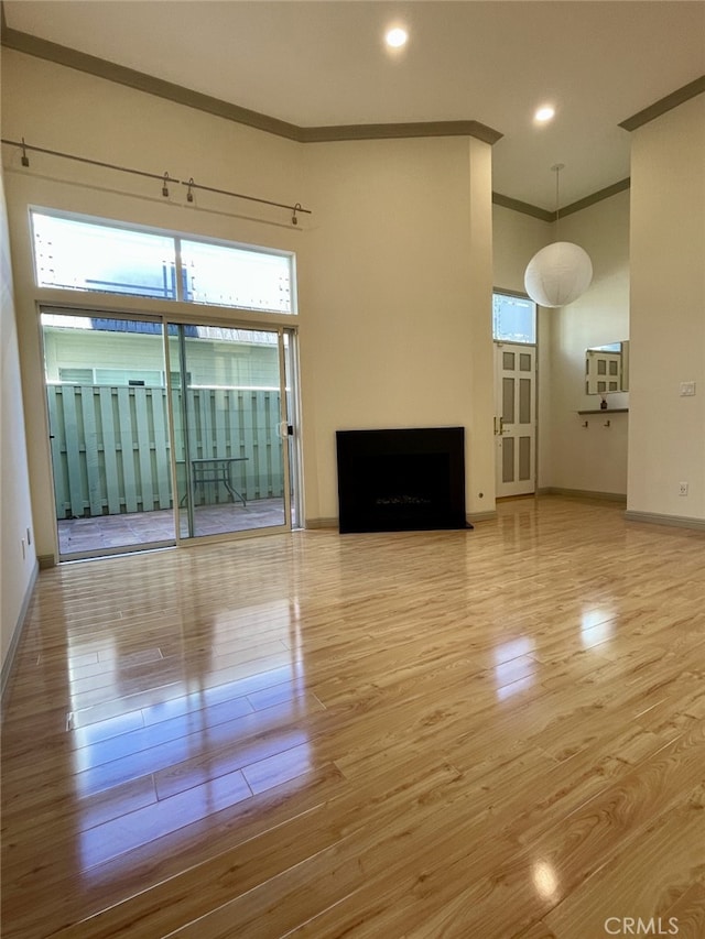 unfurnished living room featuring wood finished floors, baseboards, recessed lighting, a fireplace, and ornamental molding