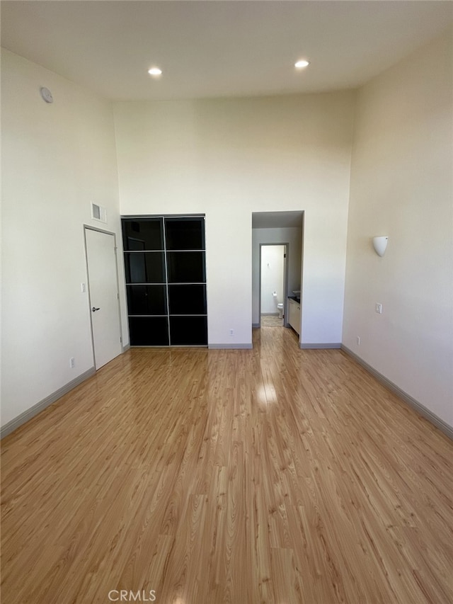 spare room featuring baseboards, visible vents, light wood finished floors, a high ceiling, and recessed lighting