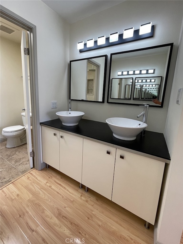 bathroom with double vanity, wood finished floors, visible vents, and a sink