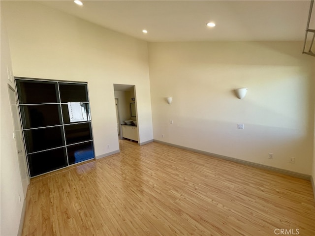 empty room featuring recessed lighting, baseboards, high vaulted ceiling, and light wood finished floors