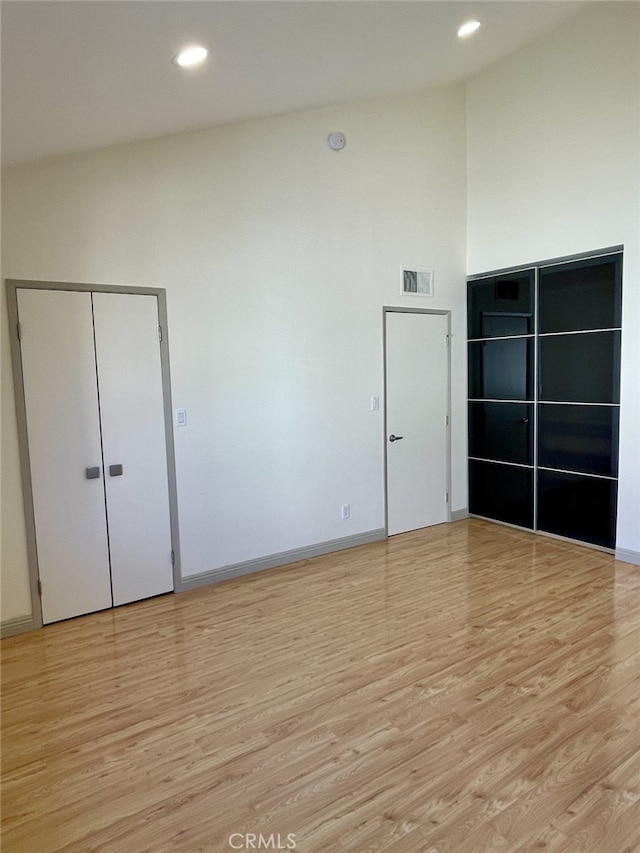 interior space featuring visible vents, baseboards, light wood-style floors, and high vaulted ceiling