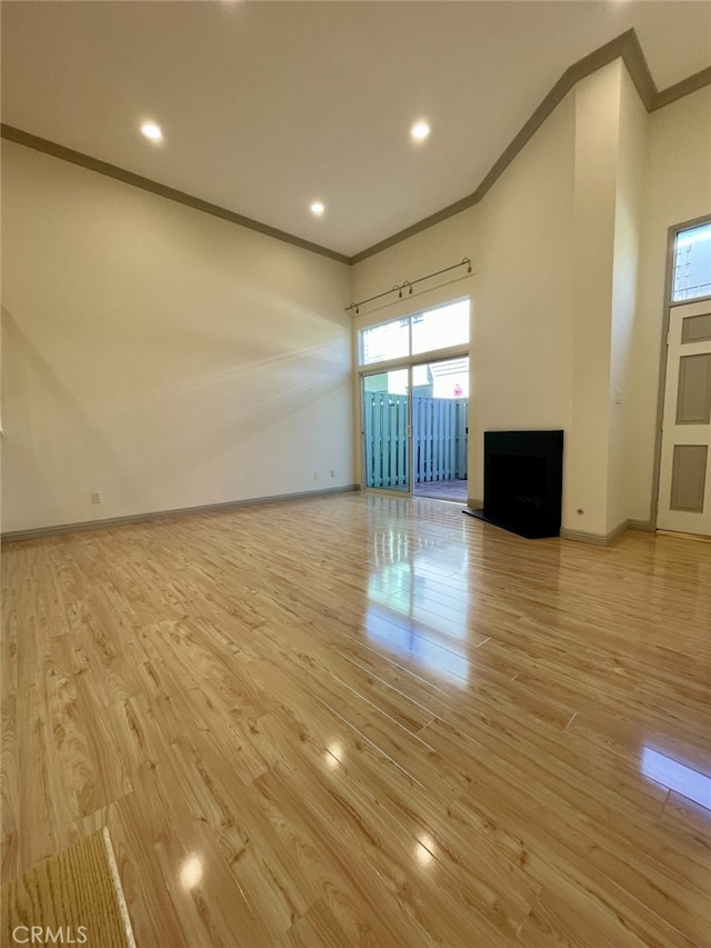 unfurnished living room with baseboards, light wood-style floors, a fireplace with raised hearth, and ornamental molding