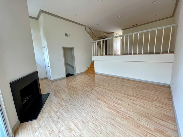 unfurnished living room with baseboards, high vaulted ceiling, ornamental molding, stairs, and light wood-style floors