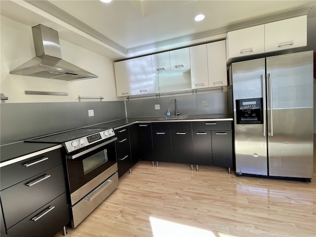 kitchen with wall chimney range hood, dark cabinets, appliances with stainless steel finishes, white cabinetry, and a sink