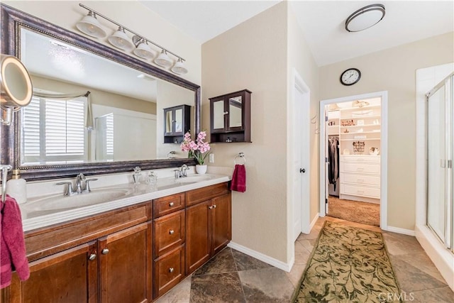 full bathroom featuring double vanity, a stall shower, baseboards, and a sink