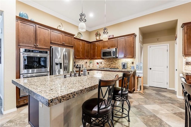 kitchen featuring tasteful backsplash, an island with sink, ornamental molding, appliances with stainless steel finishes, and a kitchen breakfast bar