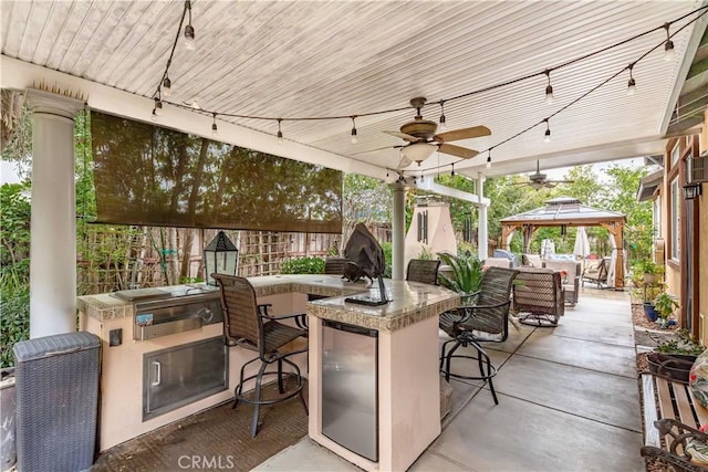 view of patio featuring a gazebo, outdoor wet bar, exterior kitchen, and a ceiling fan