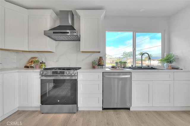 kitchen with light wood finished floors, a sink, light countertops, appliances with stainless steel finishes, and wall chimney range hood