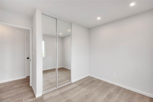 unfurnished bedroom featuring light wood-type flooring, baseboards, and a closet