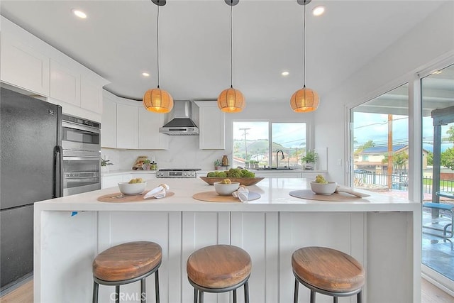 kitchen with a sink, light countertops, freestanding refrigerator, and wall chimney range hood