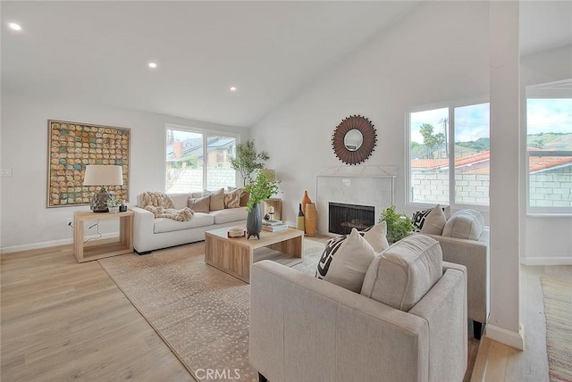 living room featuring a high end fireplace, baseboards, light wood-type flooring, recessed lighting, and high vaulted ceiling