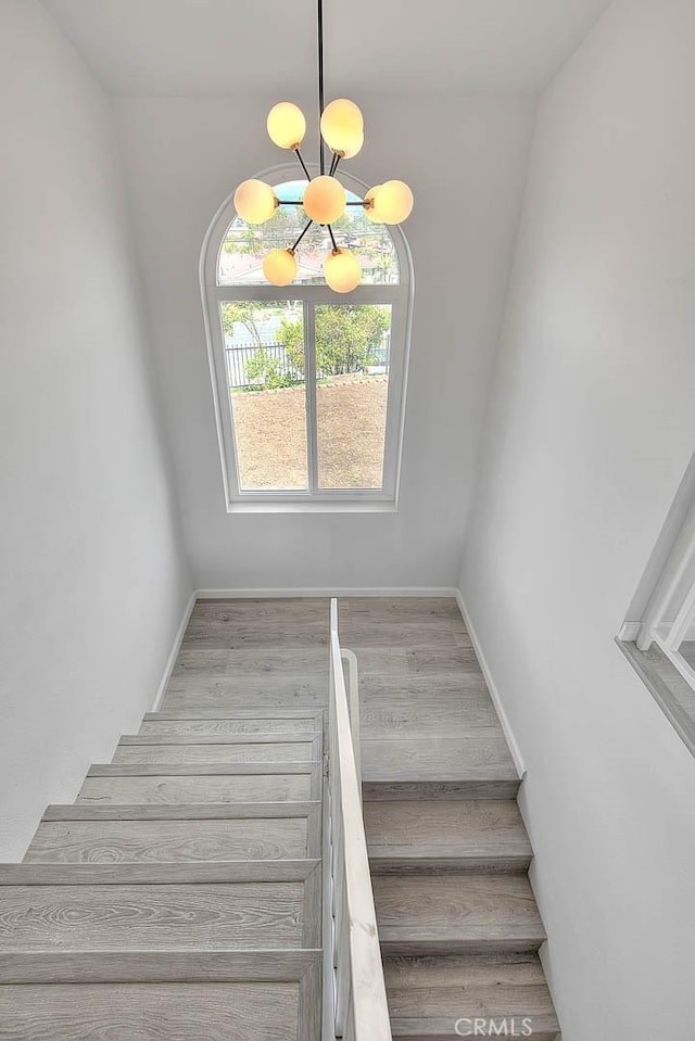 stairs with an inviting chandelier, wood finished floors, and baseboards