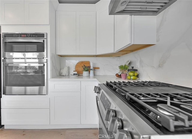 kitchen featuring range hood, stainless steel appliances, light countertops, white cabinets, and tasteful backsplash