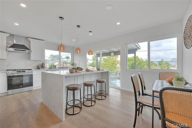 kitchen featuring a sink, light wood-style floors, wall chimney exhaust hood, and stainless steel range with electric cooktop