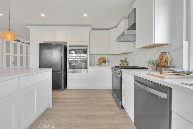 kitchen with light wood finished floors, white cabinets, stainless steel appliances, and wall chimney range hood