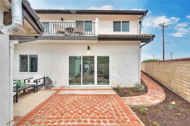 rear view of house with a balcony, fence, stucco siding, a tiled roof, and a patio area