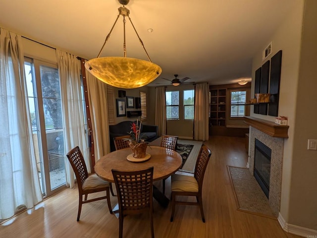 dining area featuring a fireplace with flush hearth, baseboards, light wood finished floors, and ceiling fan