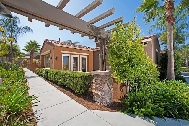 view of property exterior with a tiled roof, a pergola, and stucco siding