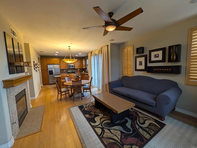 living room featuring visible vents, a tile fireplace, light wood-type flooring, and baseboards