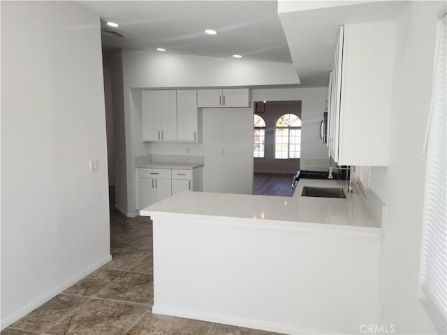 kitchen with a peninsula, recessed lighting, a sink, light countertops, and stainless steel microwave