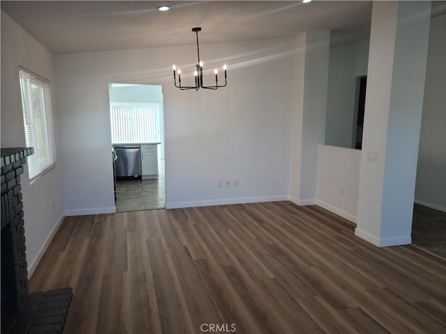 unfurnished dining area with dark wood-type flooring, a fireplace, baseboards, and a chandelier