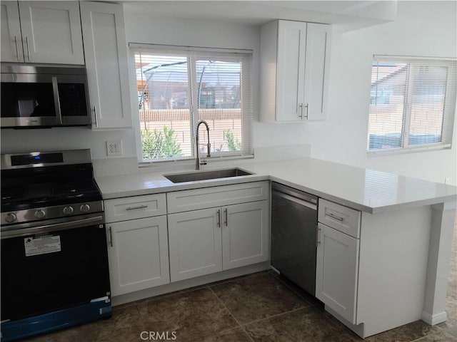 kitchen with a peninsula, a sink, stainless steel appliances, light countertops, and white cabinets