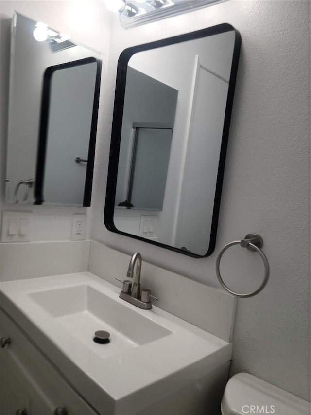 half bathroom featuring toilet, vanity, and a textured wall