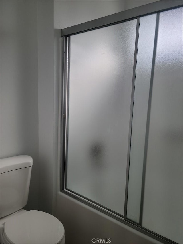 bathroom with toilet and shower / bath combination with glass door